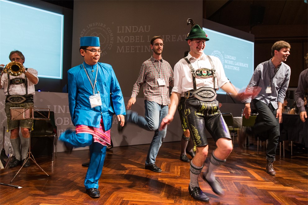 Young scientists in traditional attire dancing with Bavarian dancers at the Bavarian Evening of the 5th Meeting on Economic Sciences.